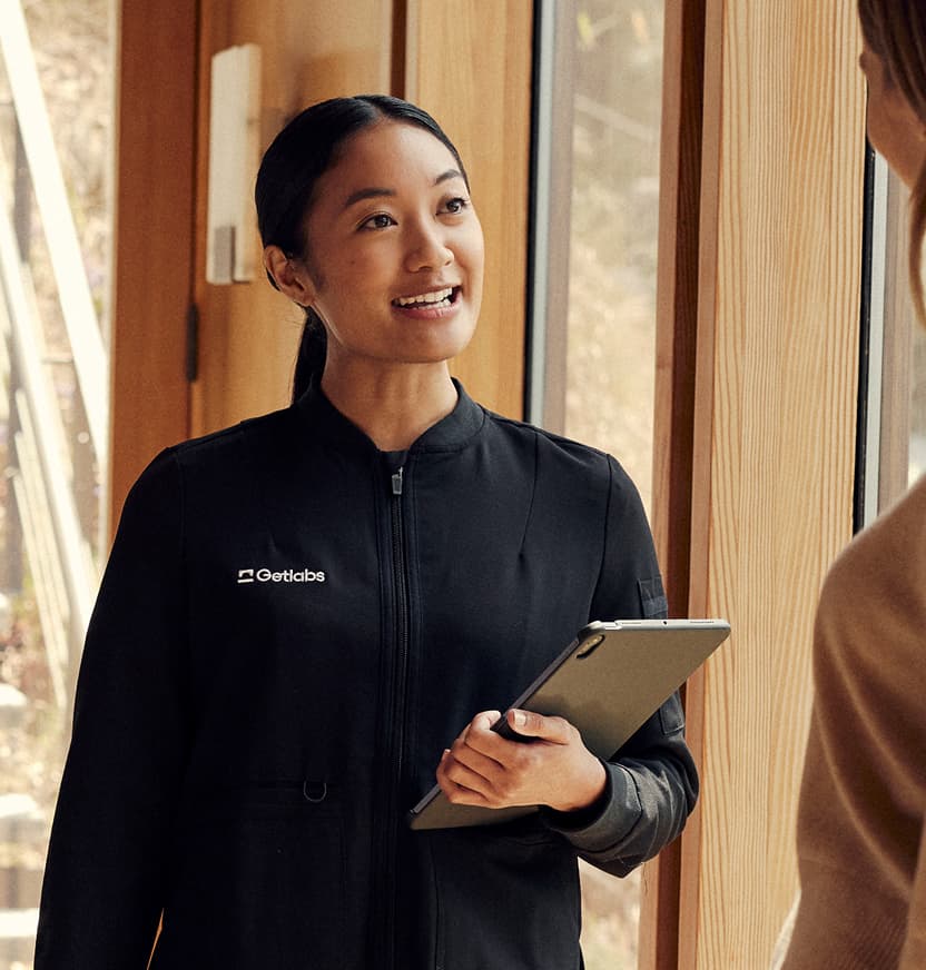 A Getlabs specialist in black scrubs holding an iPad, smiling at a patient